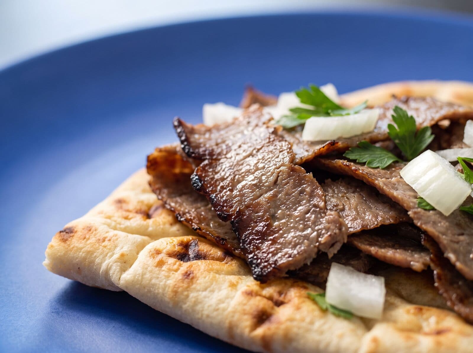 Beispielbild: Nahaufnahme von gebräuntem Dönerfleisch mit Zwiebelwürfeln und Petersilie auf Fladenbrot